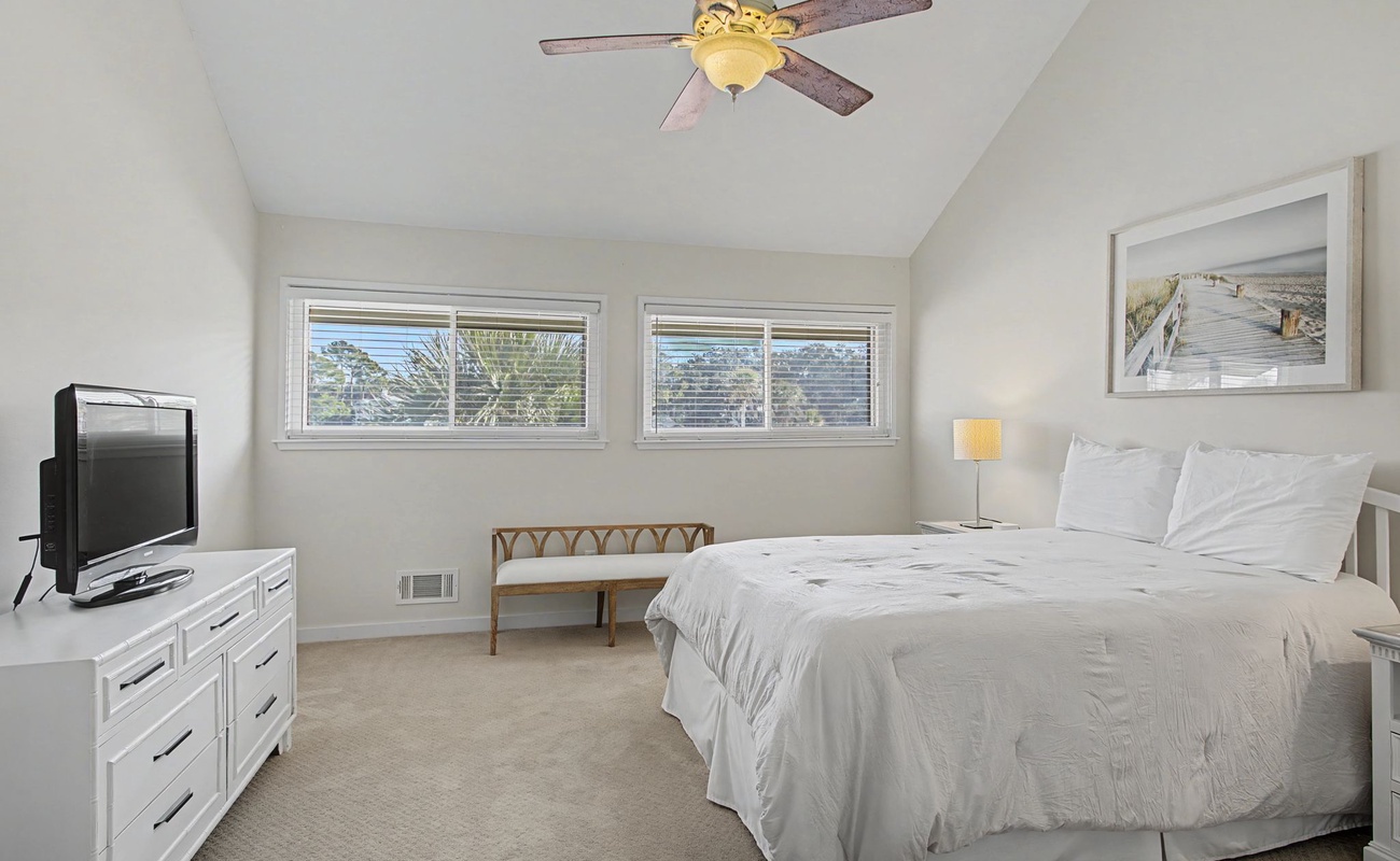 Rest in your serene bedroom with crisp white linens, gentle ceiling fan, and peaceful garden views through large windows.
