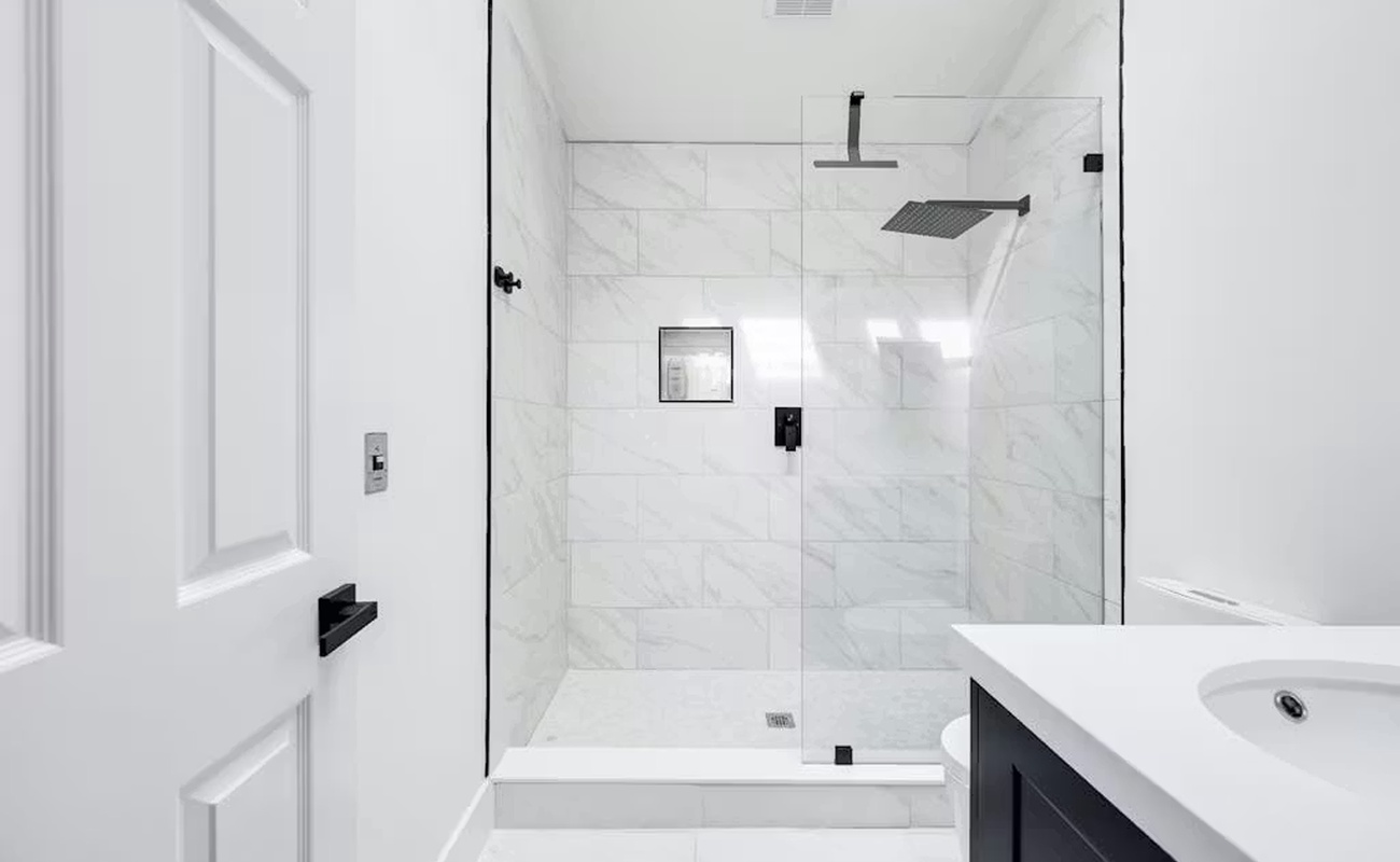 Step into your spa-like sanctuary with gleaming marble tiles, a spacious glass-enclosed shower featuring dual rainfall heads, and pristine white finishes throughout.