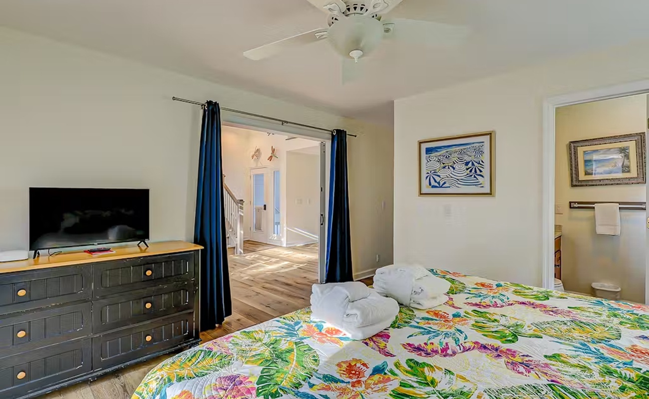 Unwind in your bright bedroom featuring tropical bedding, entertainment center, and fresh towels awaiting your arrival.