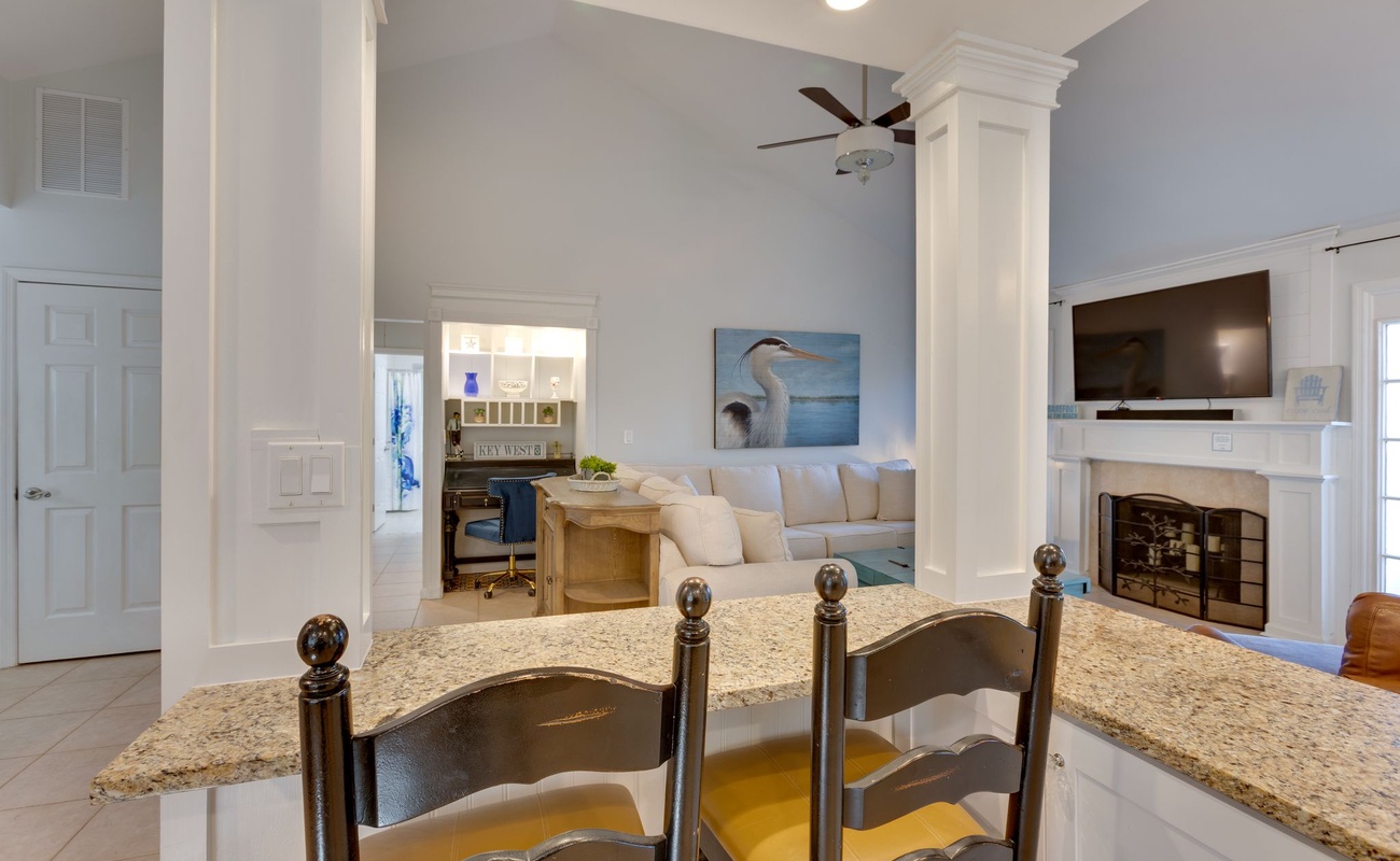 Relax in your spacious living area featuring soaring ceilings, coastal artwork, and a cozy fireplace—perfect for unwinding after beach days.