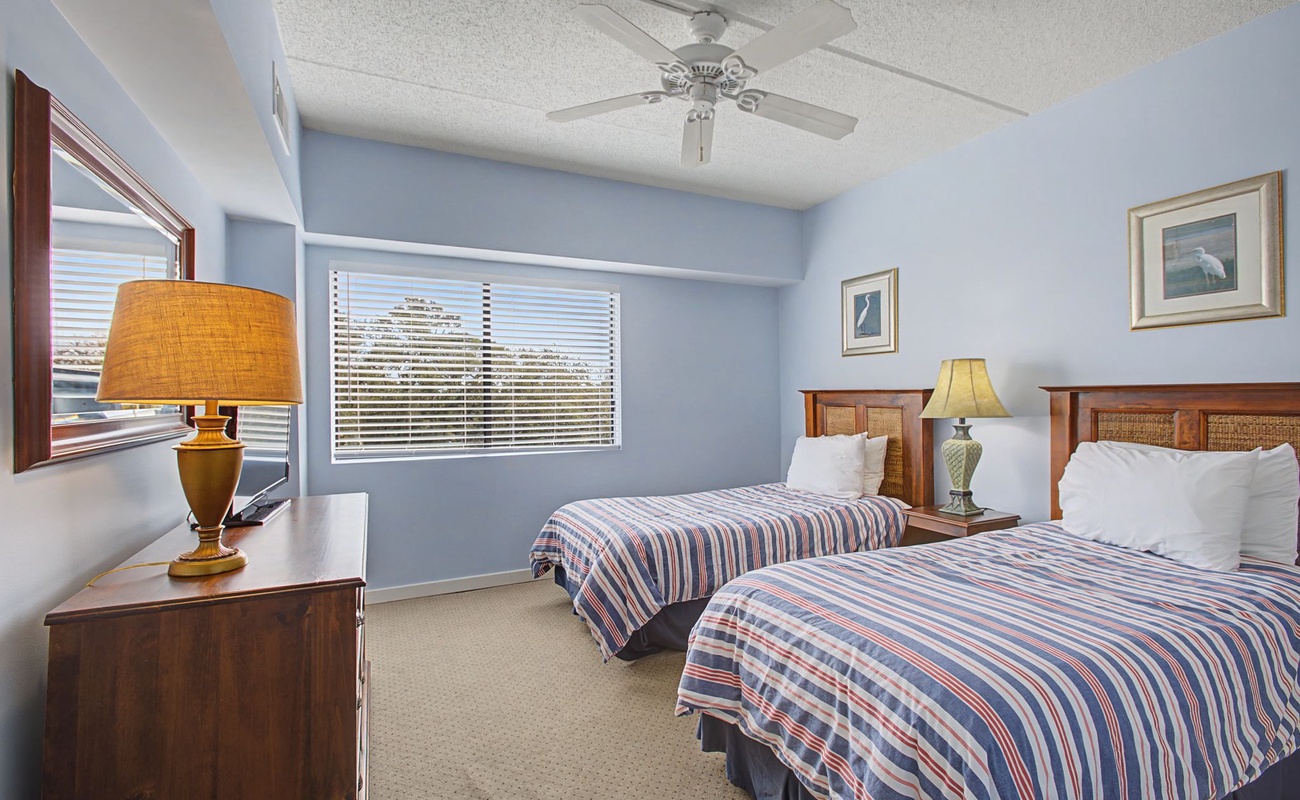 Drift off in comfort with twin beds, soft linens, and a gentle ceiling fan creating the perfect sleep sanctuary.