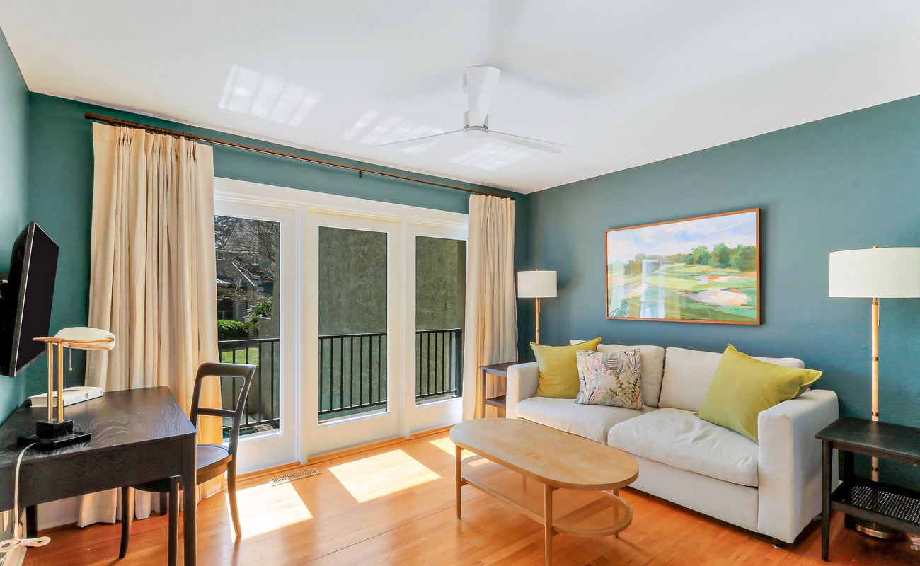 Relax in this stylish living room with plush seating, warm wood floors, and your private balcony overlooking peaceful greenery.