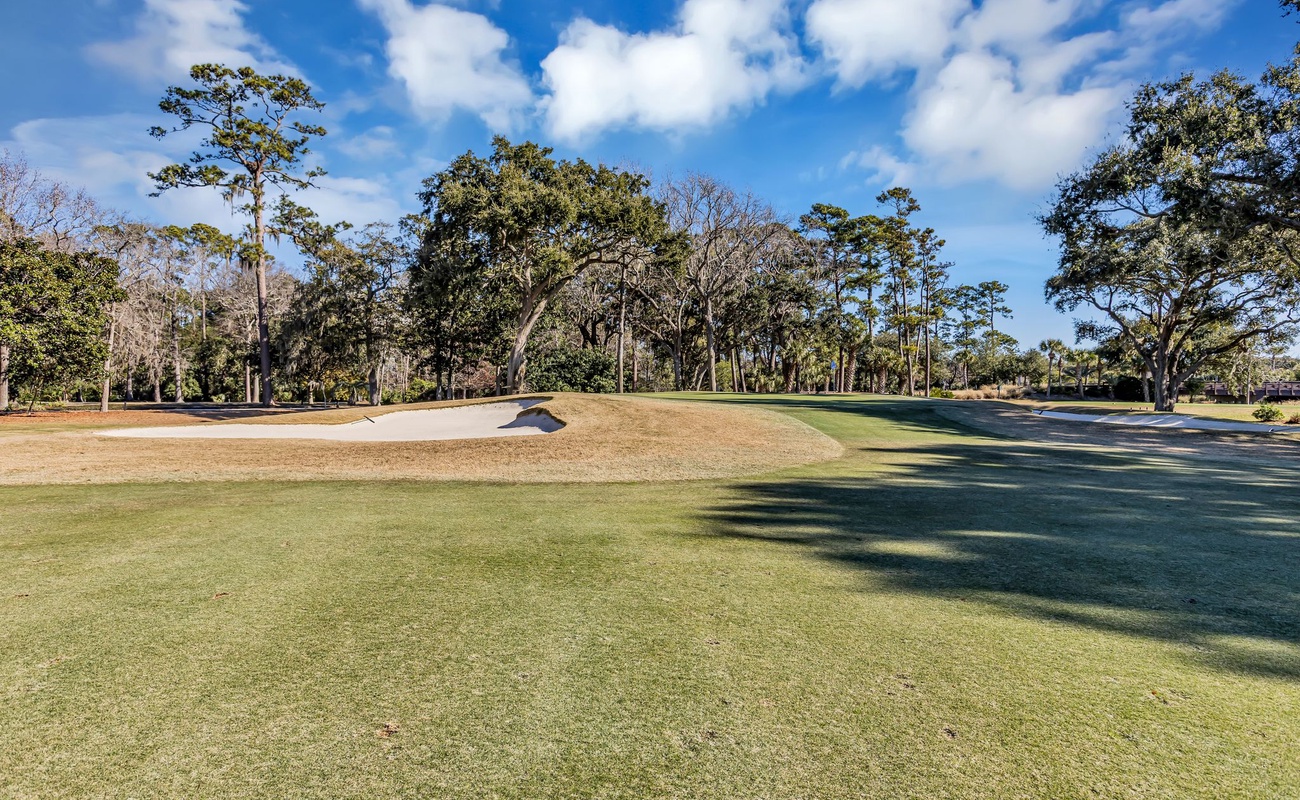 Championship golf course featuring manicured fairways and sand bunkers surrounded by mature oak trees under bright blue skies.
