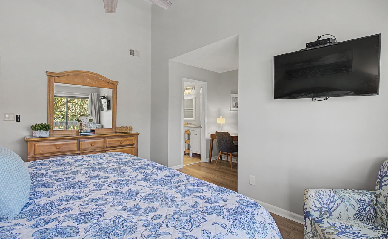 Drift off in your cozy bedroom featuring a plush blue floral bed, warm wood furnishings, and wall-mounted TV for relaxing evenings.