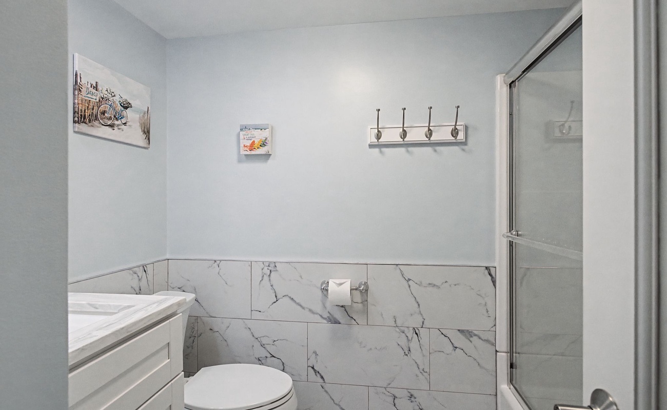 Step into your elegantly updated bathroom featuring marble-look tile, modern fixtures, and thoughtful touches like wall hooks for your convenience.