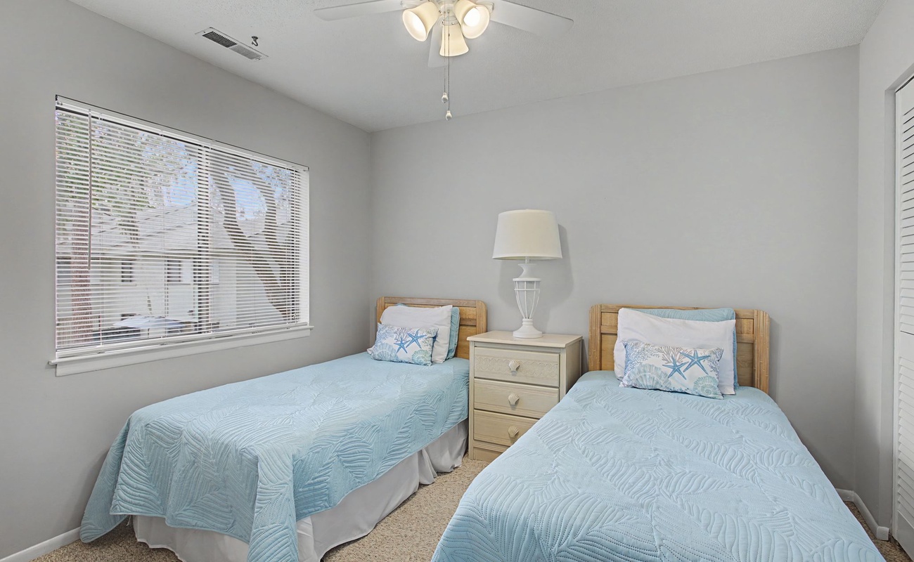 Rest peacefully in your bright twin bedroom with soft blue linens and gentle natural light streaming through the window.