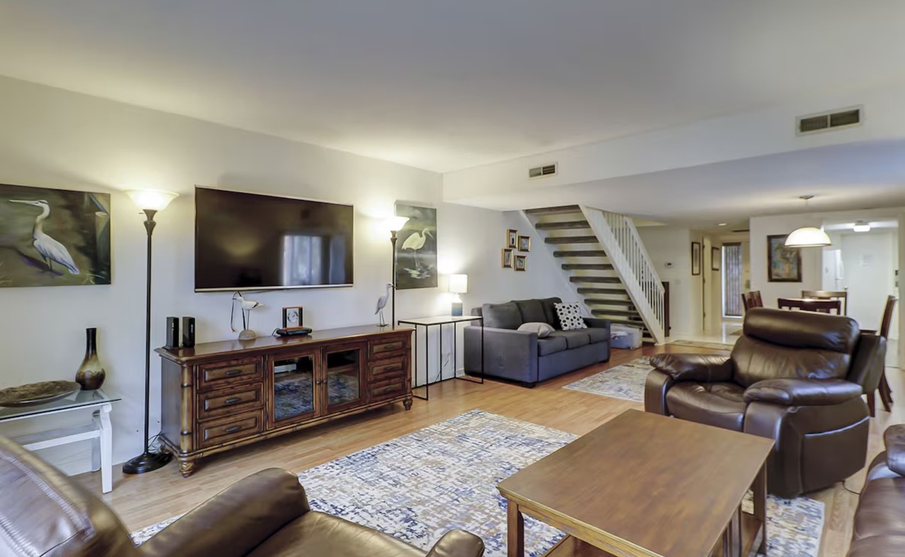 Unwind in your spacious living room with plush leather seating, entertainment center, and modern staircase leading to upper floors.