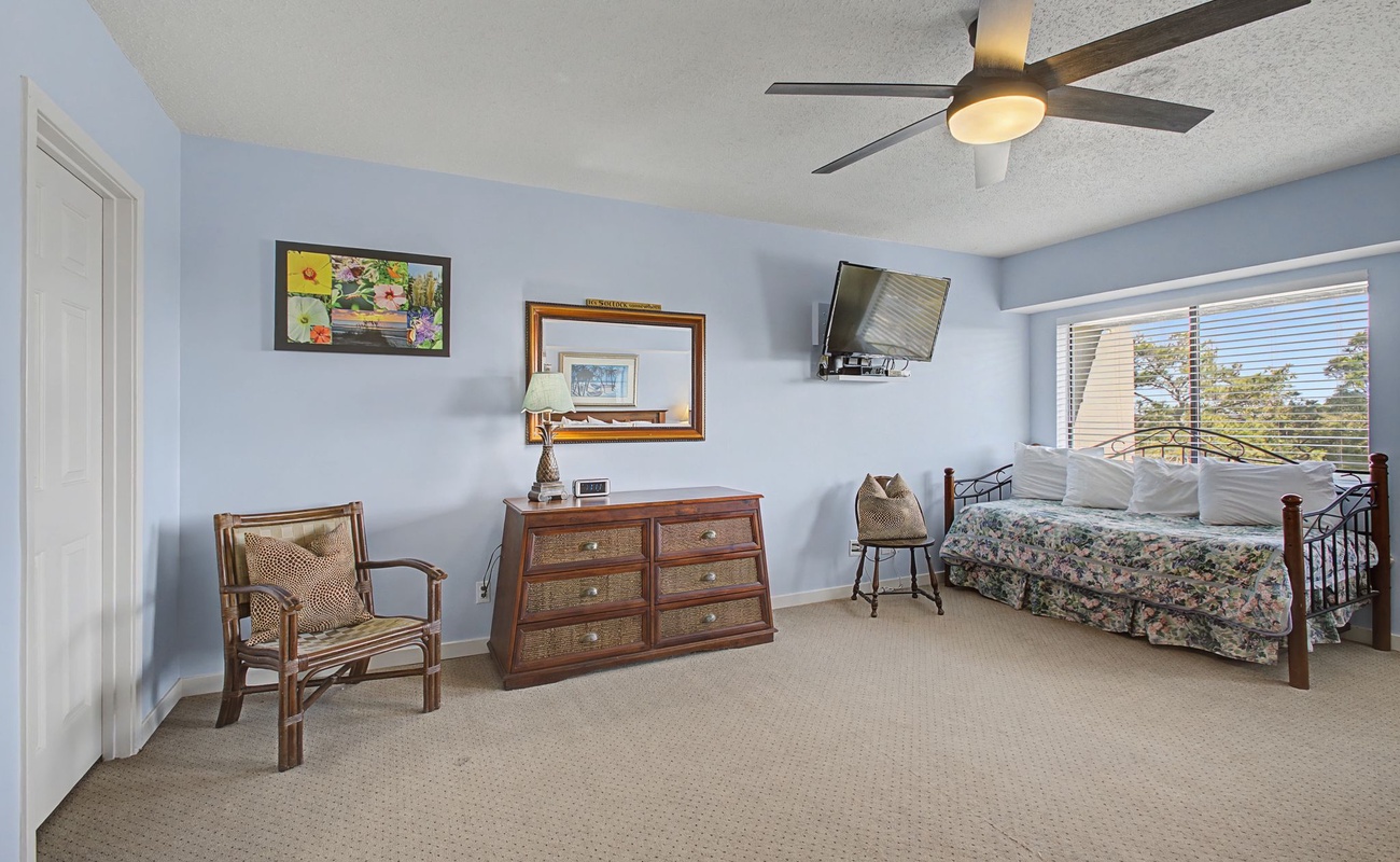 Relax in your spacious bedroom with coastal charm, featuring a ceiling fan for comfort and natural light streaming through the windows.