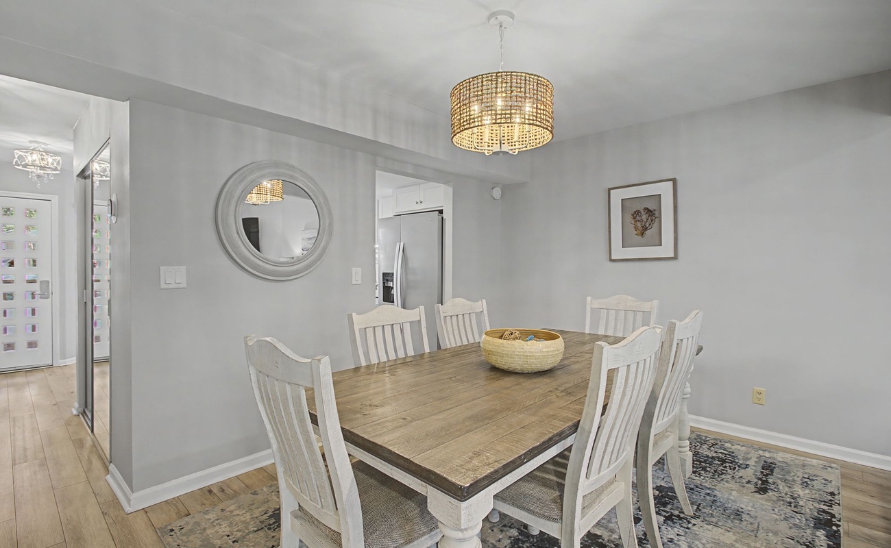 Gather around your elegant dining table where warm conversations flow under coastal-inspired chandelier light and soft natural tones create perfect dinner memories.