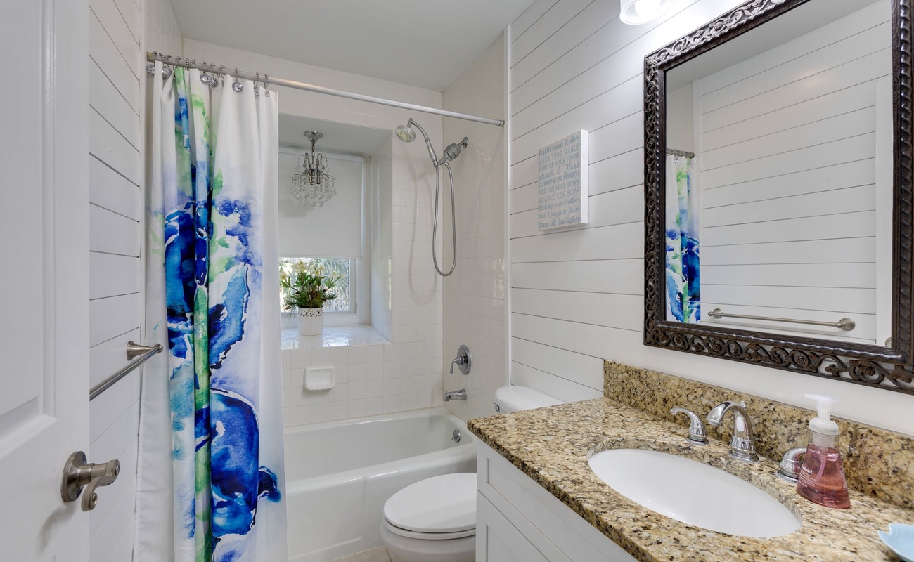 Refresh in your bright bathroom with granite counters, decorative mirror, and tub-shower combo featuring colorful curtains and coastal charm.