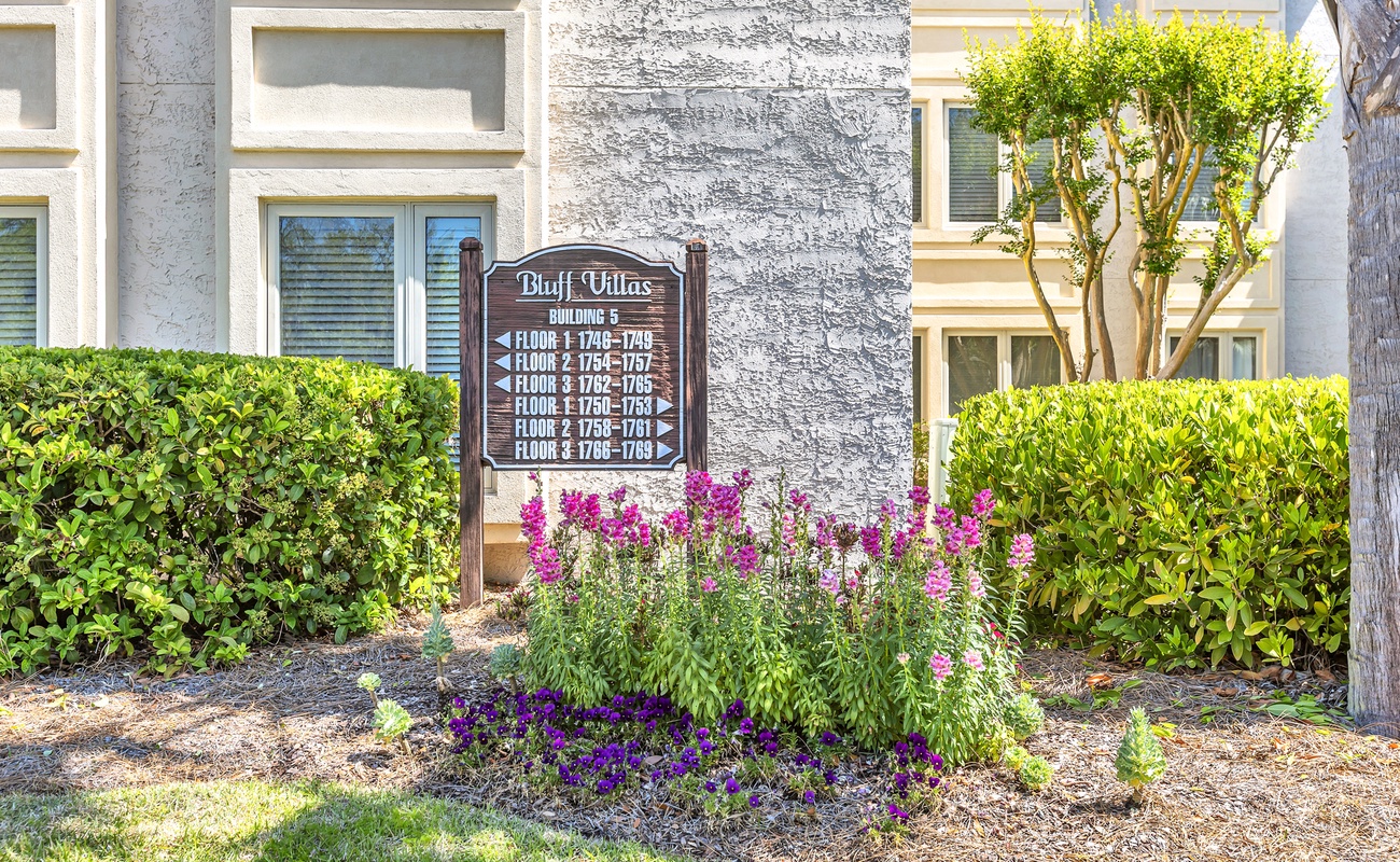 Bluff Villas Building 6 entrance marker surrounded by colorful landscaping and mature trees in a well-maintained residential setting.
