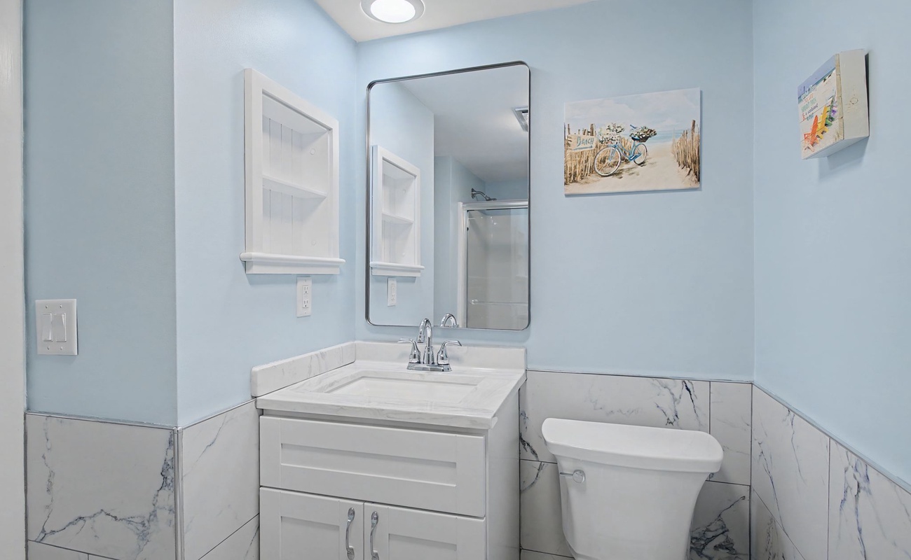 You'll love this bright, coastal-themed bathroom with elegant marble accents, thoughtful storage, and beach artwork that makes every morning feel like a getaway.