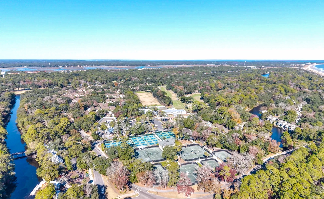 Aerial view of a resort complex nestled among lush trees, with pools and facilities visible near coastal waterways.
