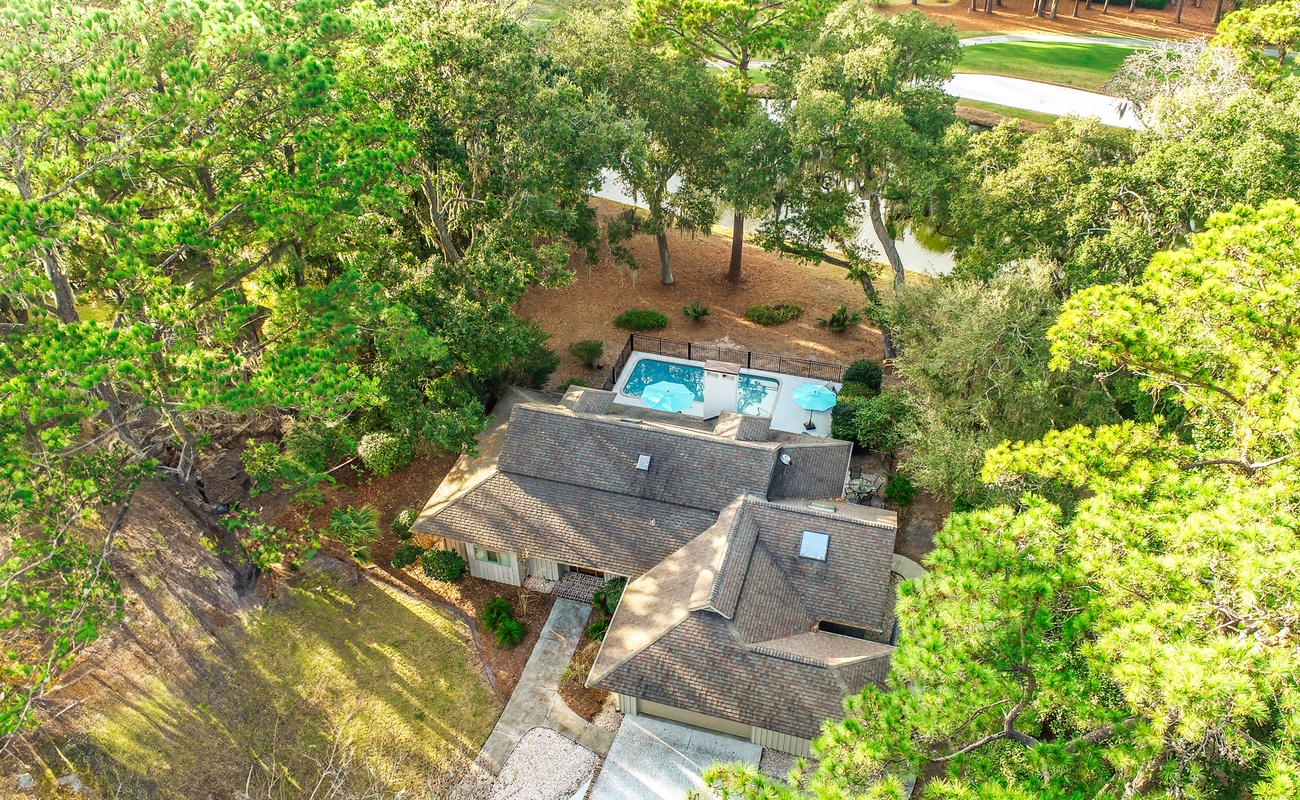 Aerial view of a charming property nestled among mature trees, featuring a sparkling swimming pool and peaceful residential setting.