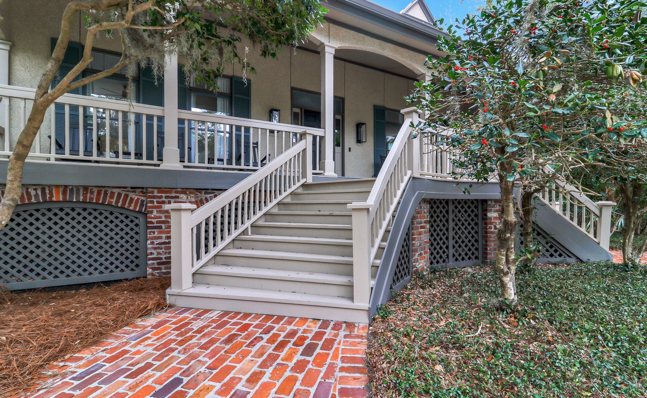 A charming Lowcountry exterior with a grand front porch, brick steps, and a sweeping driveway, all nestled beneath mature trees for a serene island welcome.