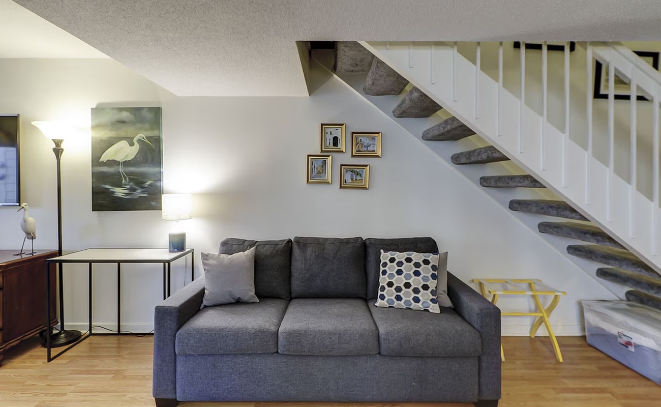 Unwind in your stylish living room featuring a plush sofa beneath beautiful coastal artwork and modern stairs.