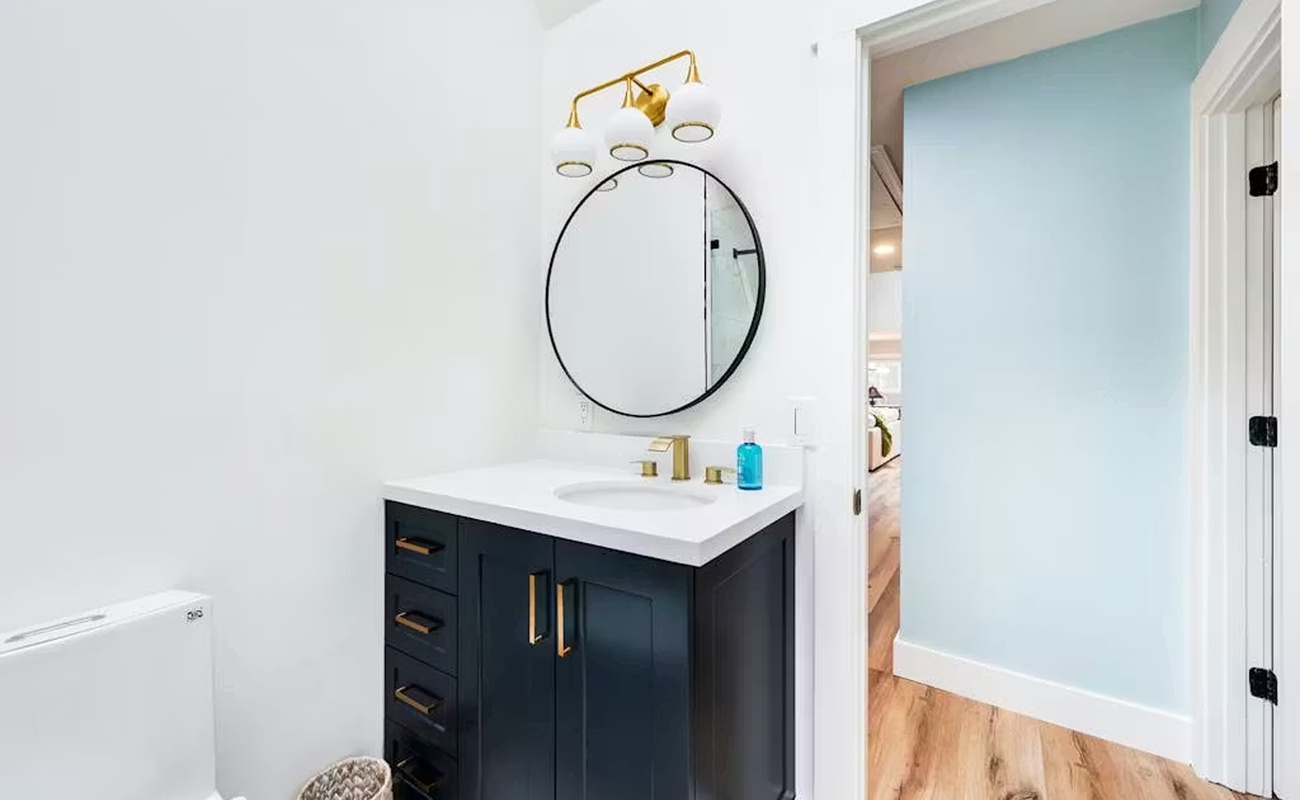 Step into this elegant bathroom featuring a striking navy vanity with brass fixtures and a sophisticated round mirror.