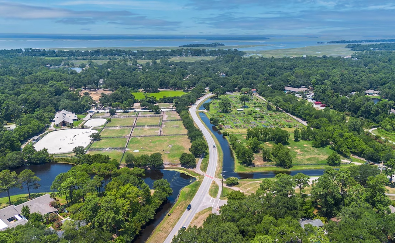 Aerial view showcasing the property's scenic coastal location, surrounded by lush forests and winding waterways leading toward the distant shoreline.