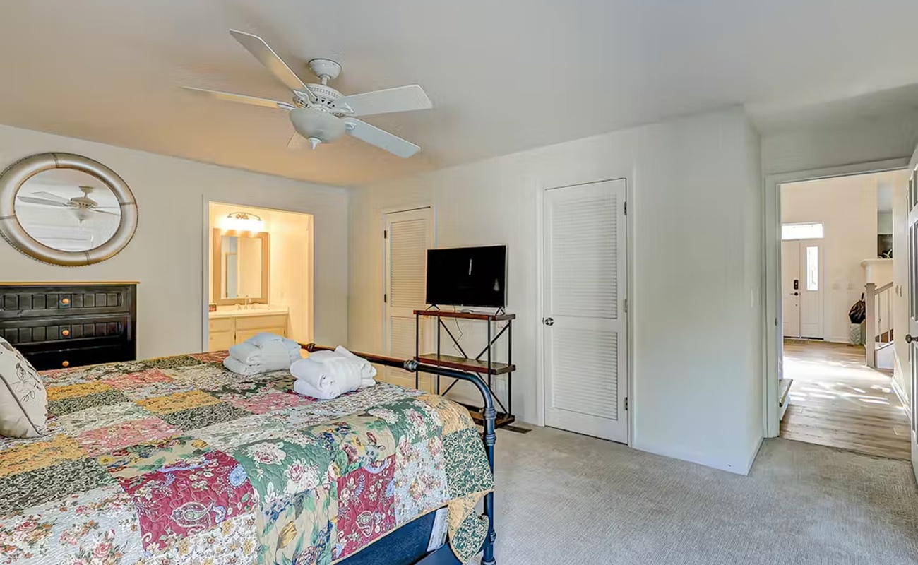 Relax in your spacious bedroom featuring a ceiling fan, TV, and patchwork quilt bedding that adds charming character to your restful retreat.