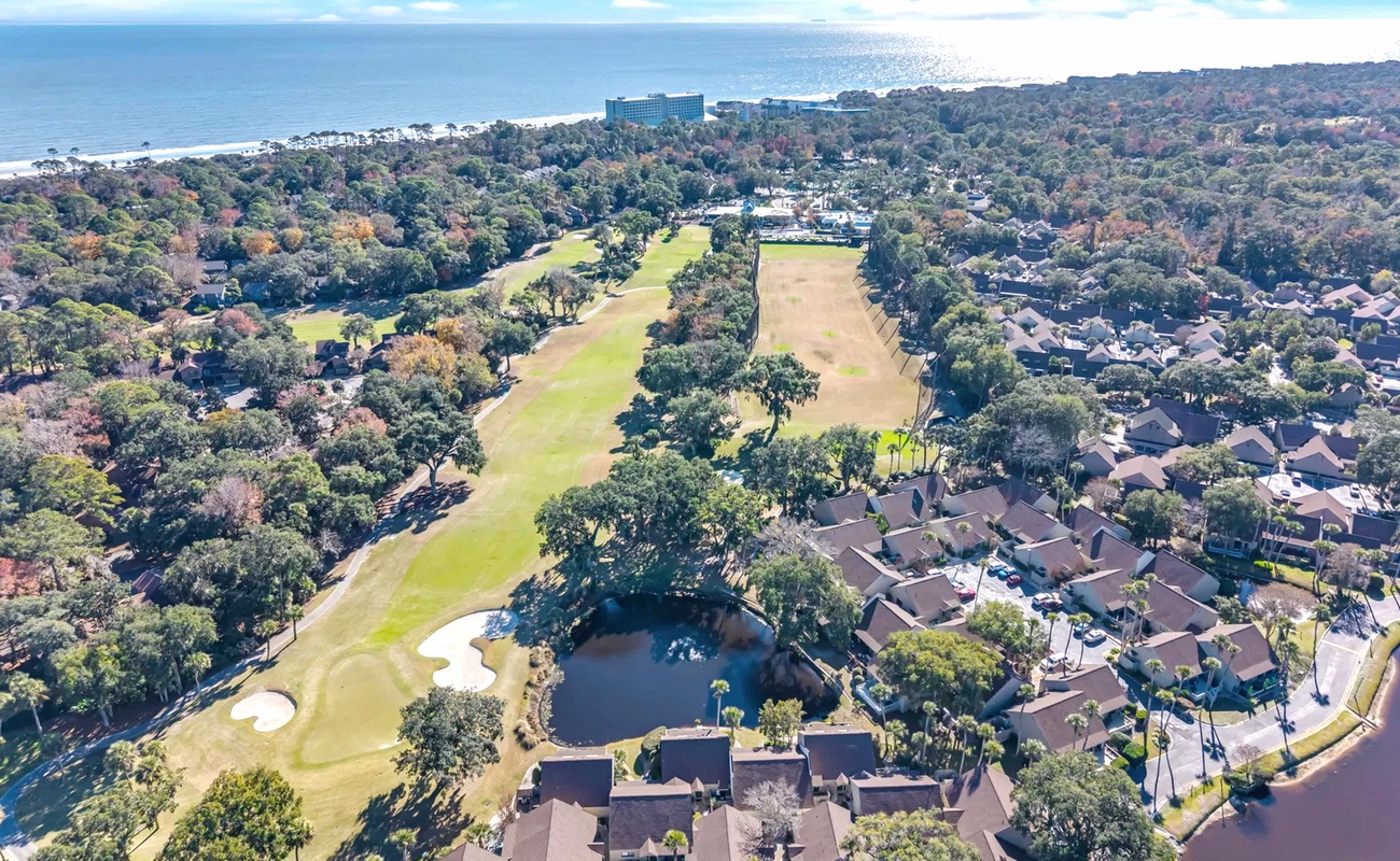 Aerial view of a stunning coastal community featuring golf course fairways, waterfront homes, and pristine beachfront access.