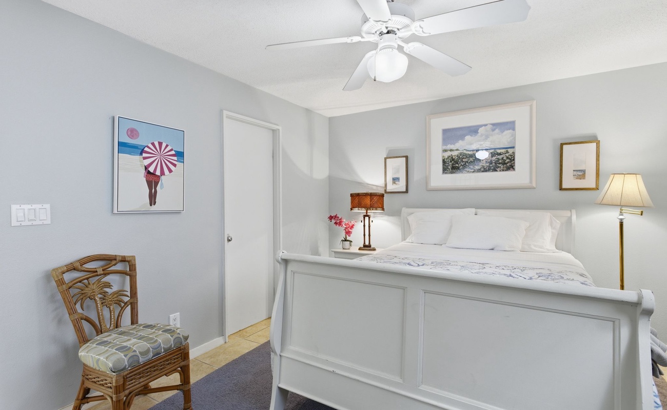 Rest peacefully in your serene bedroom featuring a comfortable queen bed, coastal artwork, and gentle ceiling fan breeze.