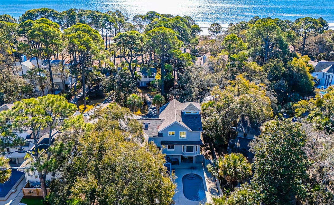 Stunning aerial view of the coastal property nestled among lush trees, just steps from pristine beaches and sparkling ocean waters.