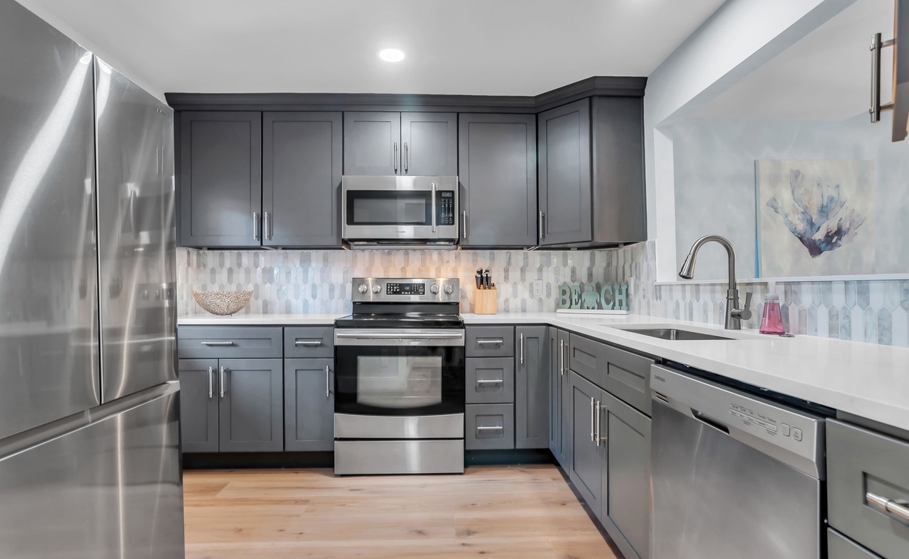 Cook your favorite meals in this fully equipped modern kitchen featuring sleek gray cabinets, stainless steel appliances, and elegant quartz countertops.