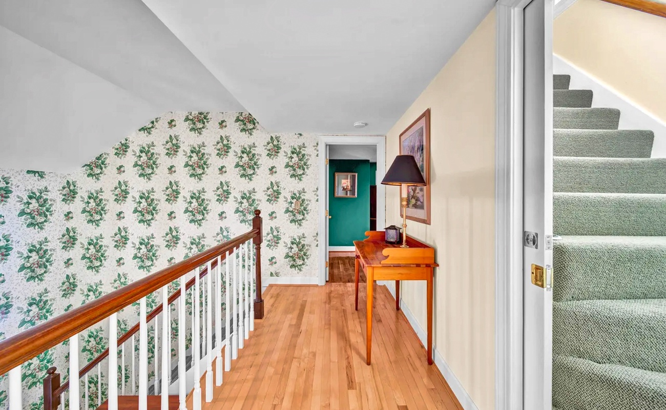 Your private upstairs hallway combines vintage charm with modern comfort—warm wood floors, floral wallpaper, and thoughtful furnishings create a welcoming retreat.