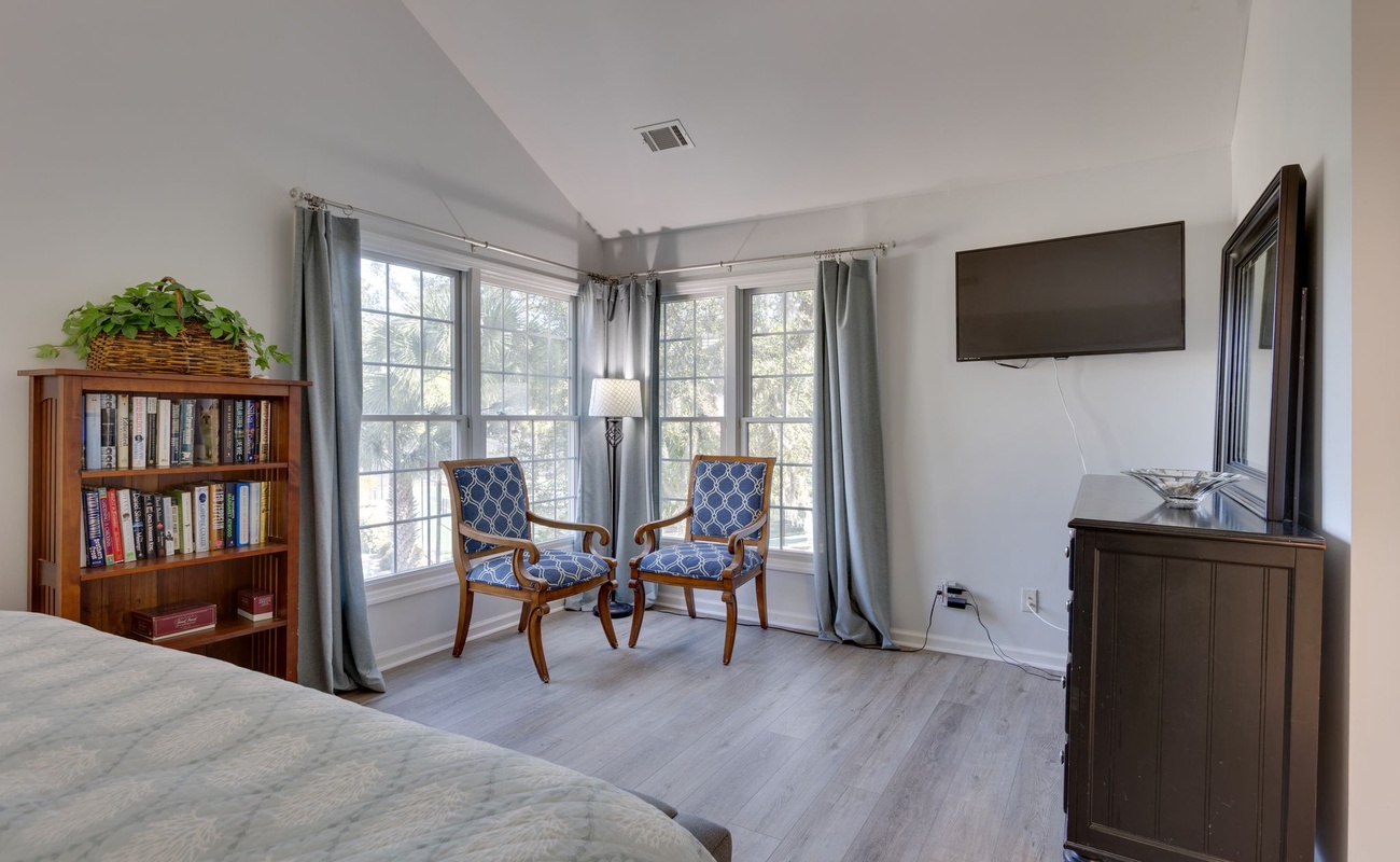 Relax in your bright bedroom featuring elegant seating by large windows, a cozy reading nook, and peaceful treetop views.