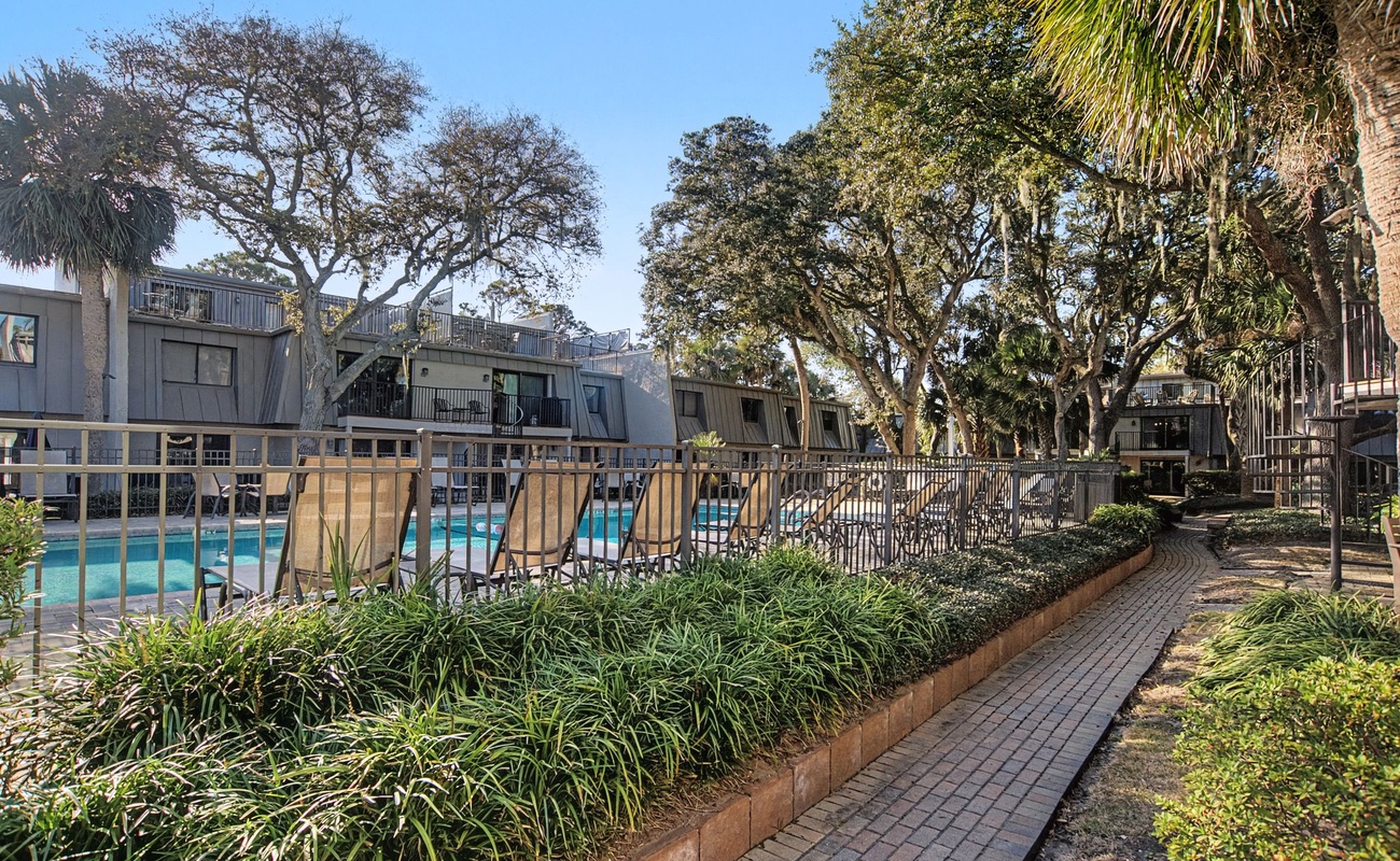 Property walkway leads through landscaped gardens toward the pool area, surrounded by mature trees and tropical plantings.
