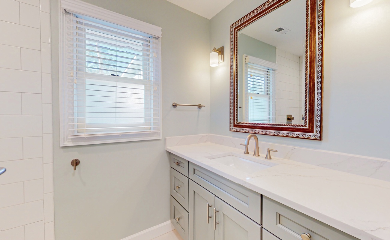 Step into your spa-like bathroom with elegant marble countertops, crisp white cabinetry, and natural light streaming through plantation shutters.