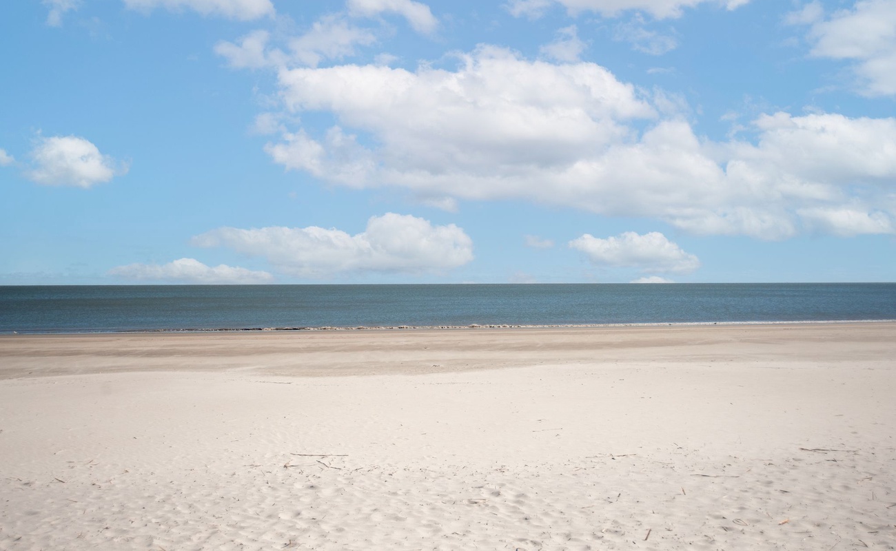Pristine sandy beach stretches endlessly under dramatic cloudy skies, with calm ocean waters creating the perfect coastal backdrop.