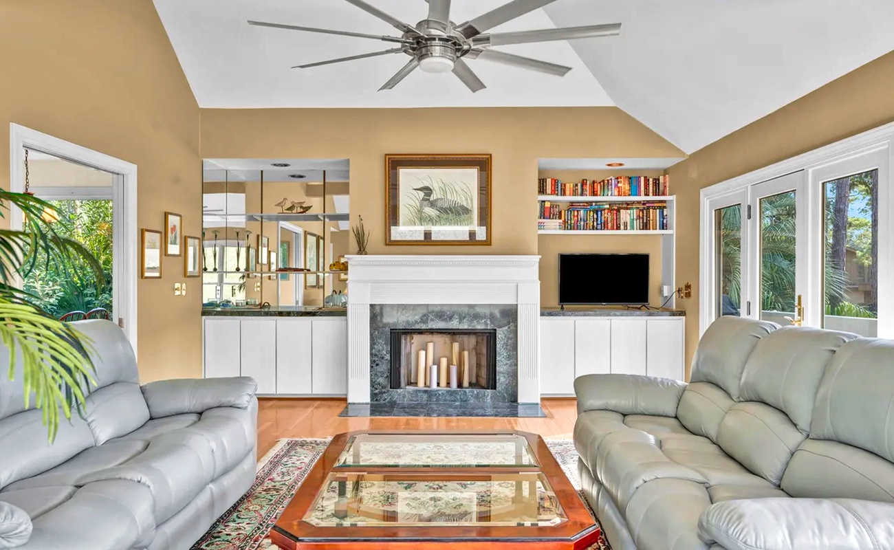 Sink into plush leather sofas by your elegant fireplace, surrounded by built-in bookshelves and tropical garden views.