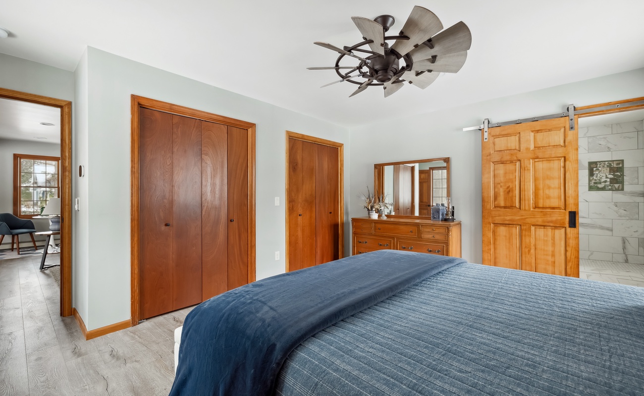 This inviting bedroom blends warm wood tones, soft blue hues, and a stunning farmhouse-style fan for the perfect retreat. Would you love to wake up here?