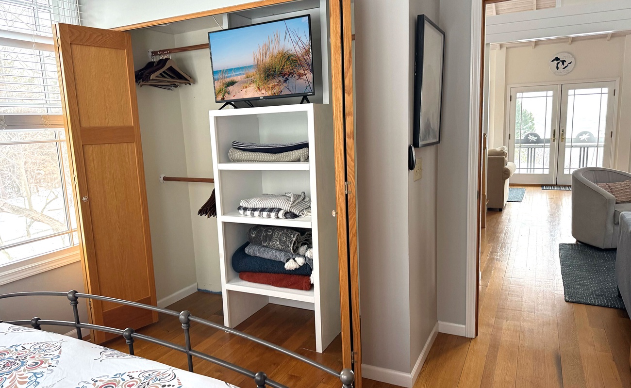 Bedroom 1 closet with built-in shelving, hangers, and a TV for added convenience.
