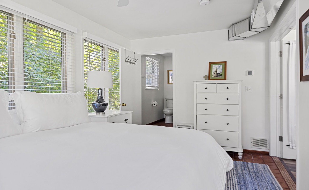 Clean lines and calming whites create a serene escape in this bedroom, complete with a spacious dresser and a cozy corner for relaxation.