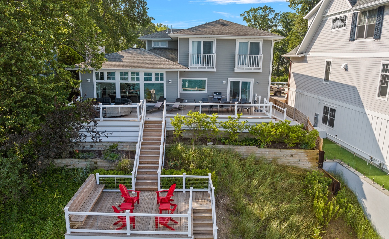 A stunning waterfront property featuring multi-level decks and modern coastal architecture surrounded by lush natural landscaping.