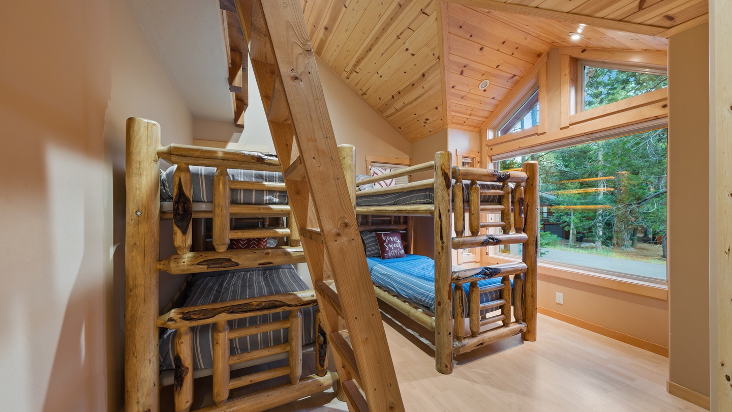 Rustic log bunk beds with handcrafted details create a cozy, cabin-style sleep space. Natural light pours in through large windows overlooking peaceful greenery, making bedtime feel like an adventure.