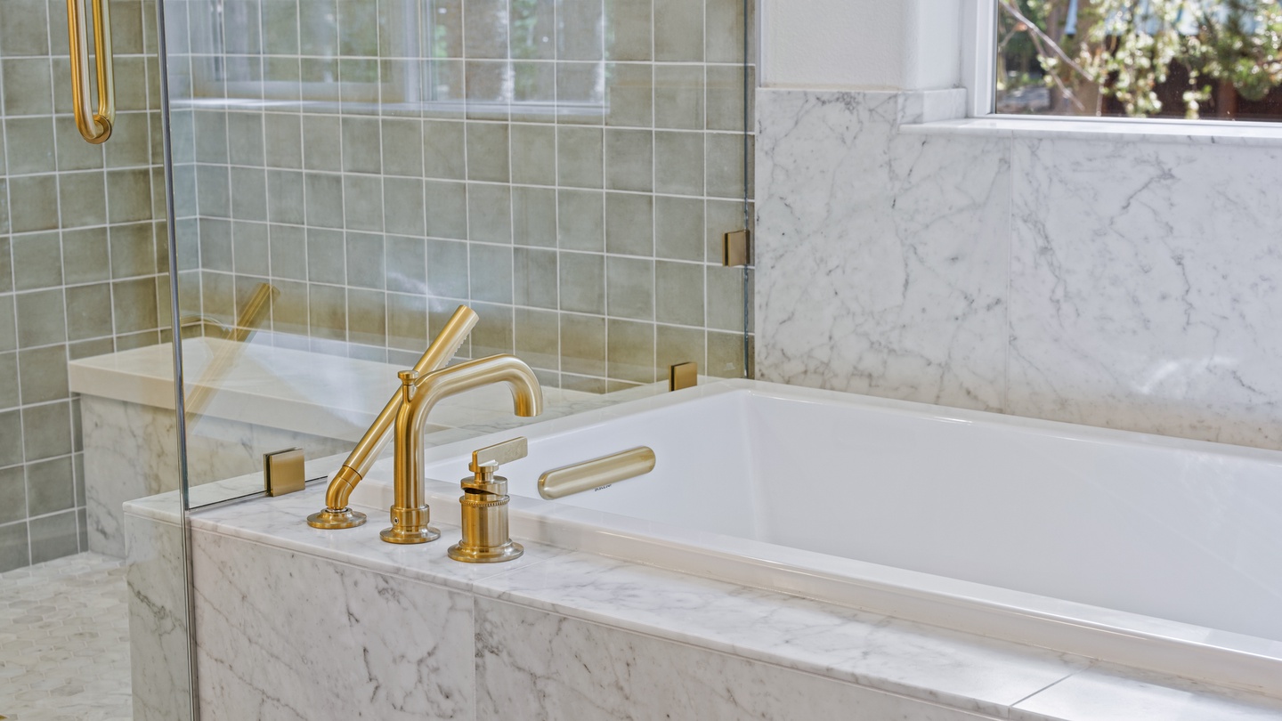 Sink into this elegant marble soaking tub with gold-accented fixtures. The separate glass-enclosed shower and soft natural light from the window create your perfect spa-like retreat.