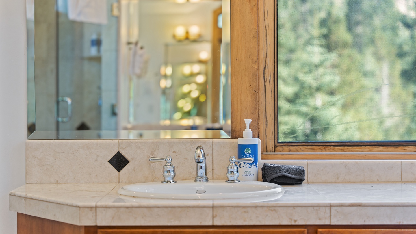 Step into your private bathroom, where natural light filters through the window revealing peaceful forest views. The clean vanity, gleaming fixtures, and thoughtfully stocked amenities create your perfect space to unwind and refresh.