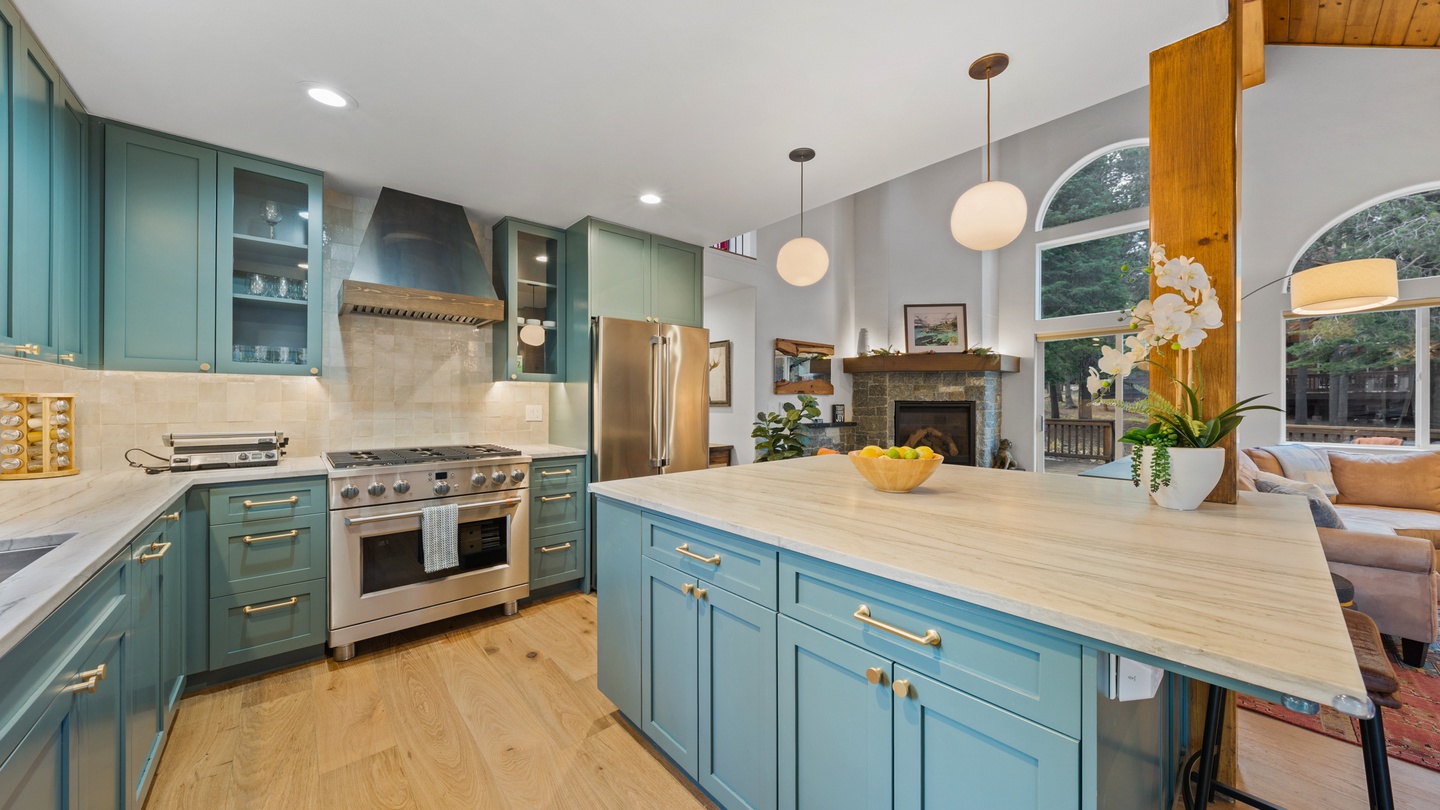 Step into a light-filled chef's kitchen where soothing teal cabinetry meets warm wood floors, inviting you to gather around the spacious island. Sunlight streams through arched windows as you prepare meals on professional-grade appliances.