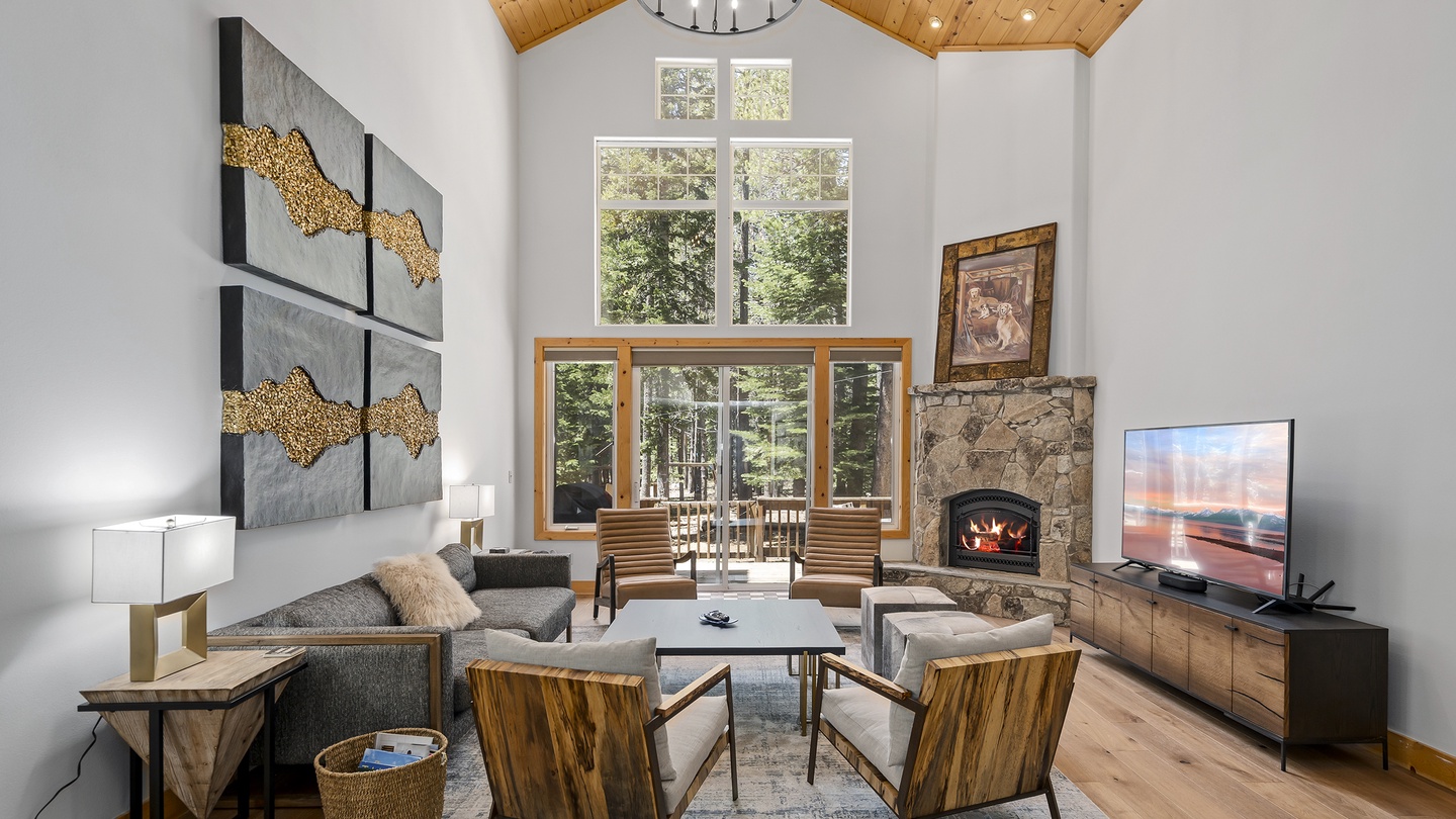 Relax in this inviting living room with soaring vaulted wood ceilings, cozy stone fireplace, and stunning views through floor-to-ceiling windows that frame the surrounding forest.