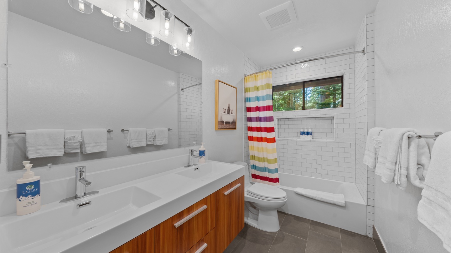 Step into your bright, modern bathroom featuring a spacious tub with fresh white subway tile, crisp towels, and a cheerful striped curtain—a refreshing space to unwind after your adventures.