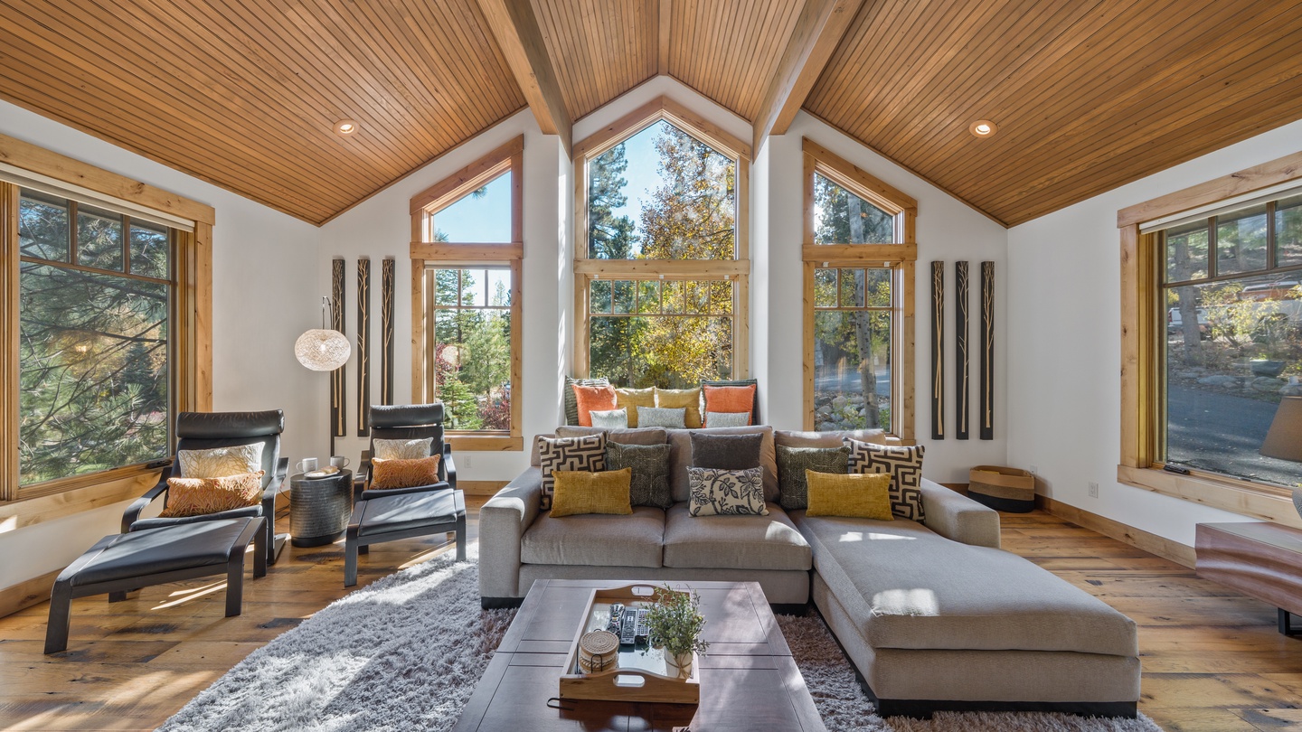 Sink into plush seating beneath soaring wood ceilings as natural light floods through floor-to-ceiling windows, framing serene forest views that bring the outdoors right to your retreat.