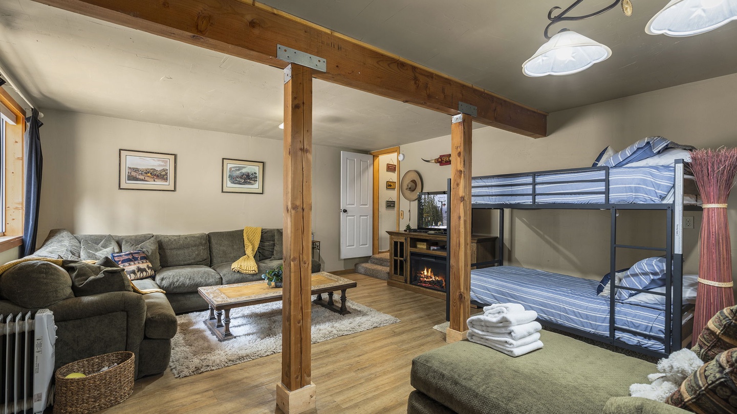 Cozy open-plan living with rustic beams, plush seating, and bunk beds—perfect for families seeking comfort and mountain charm.