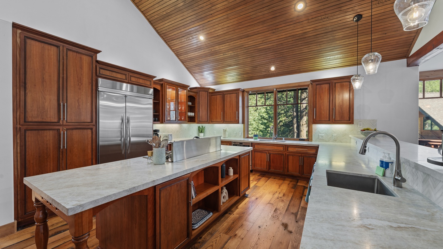 Gourmet kitchen with rich wood cabinetry, elegant marble countertops, and top-tier appliances. Sunlight streams through oversized windows beneath soaring wood-paneled ceilings.