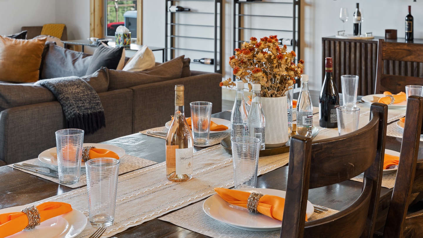 Step into your open-concept retreat, where a beautiful dining table is set for shared meals and the cozy living area invites relaxation, all bathed in natural light from tall windows.