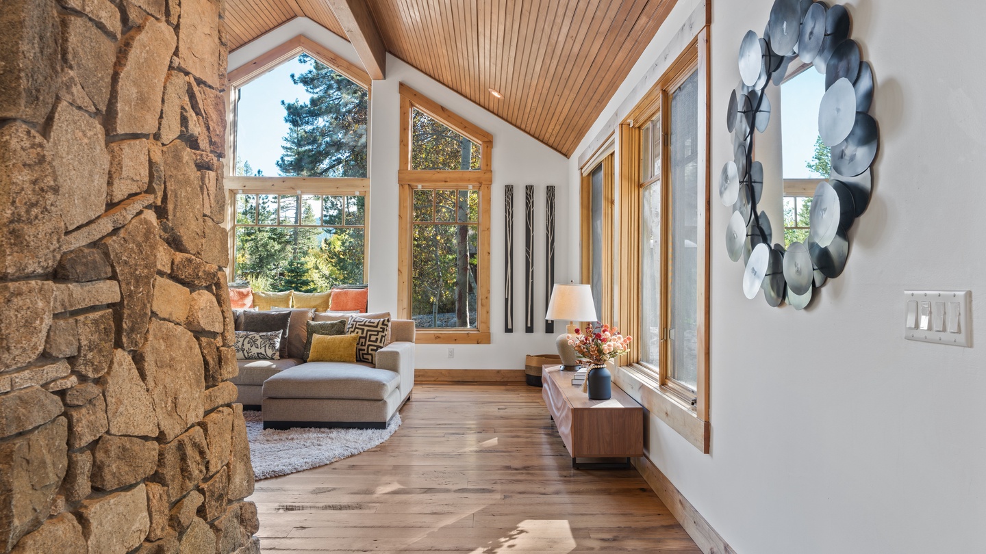 A bright, spacious living room with soaring ceilings and a stunning stone feature wall welcomes you. Large windows frame lush mountain views, while warm wood floors and contemporary décor create an inviting, peaceful retreat.