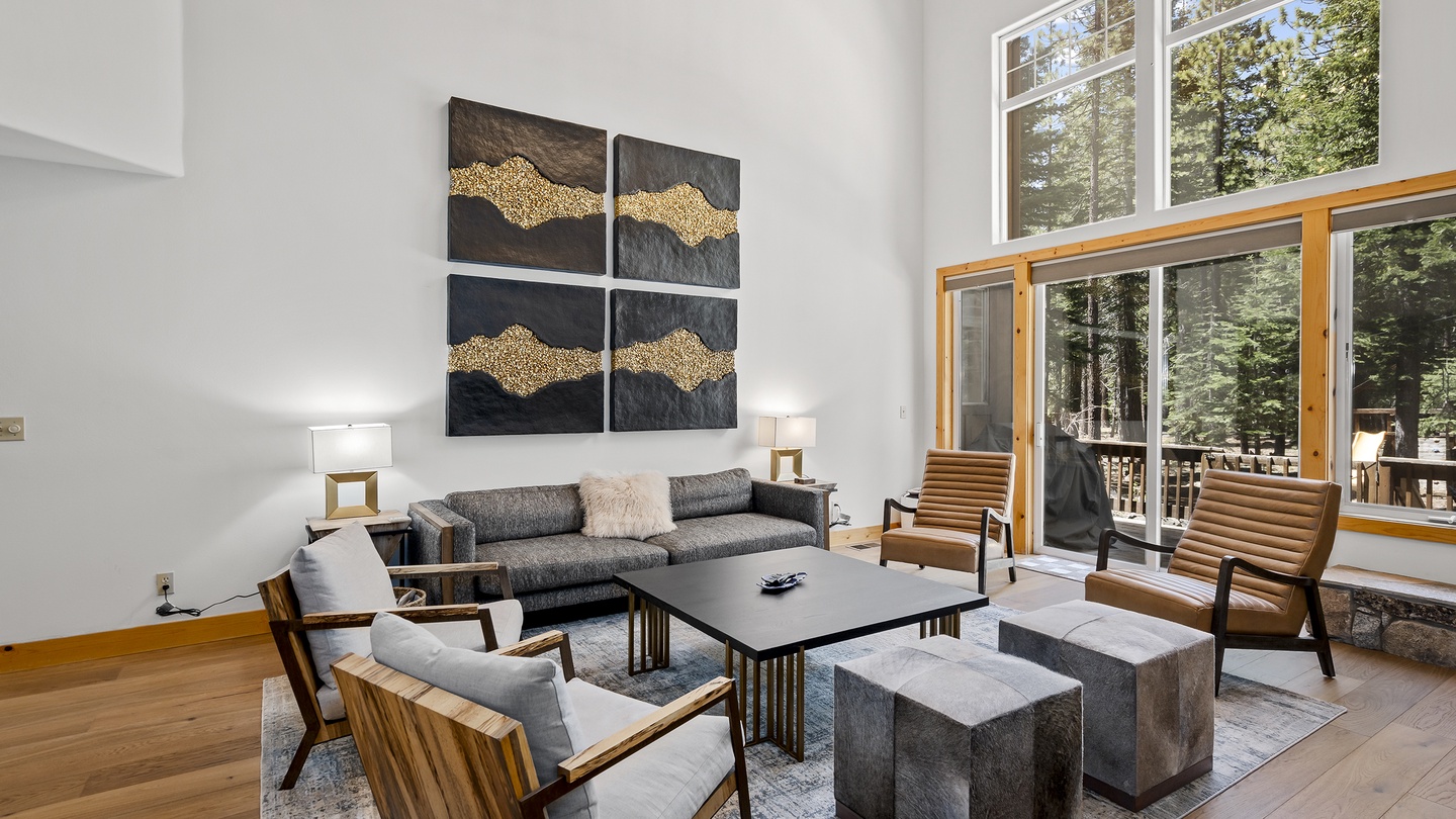Picture yourself unwinding in this bright, airy living room with soaring ceilings and natural light streaming through floor-to-ceiling windows framing lush forest views—your perfect retreat after a day of adventure.