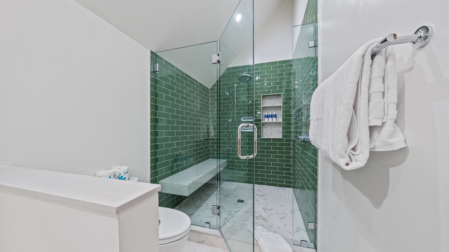 Step into your private bathroom where glossy green subway tiles and a spacious walk-in shower create a fresh, spa-like retreat. Plush towels await after every rinse.